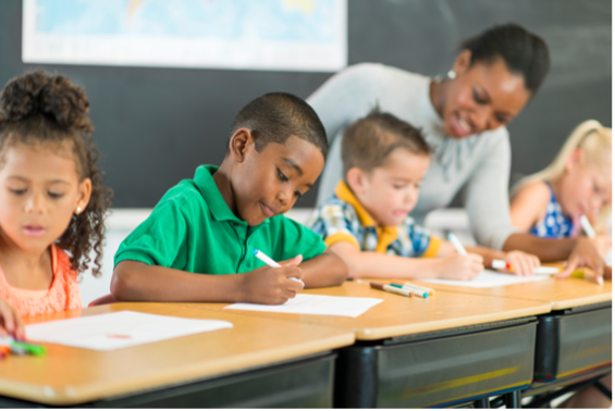 Students work at their desks while the teacher checks in with students.